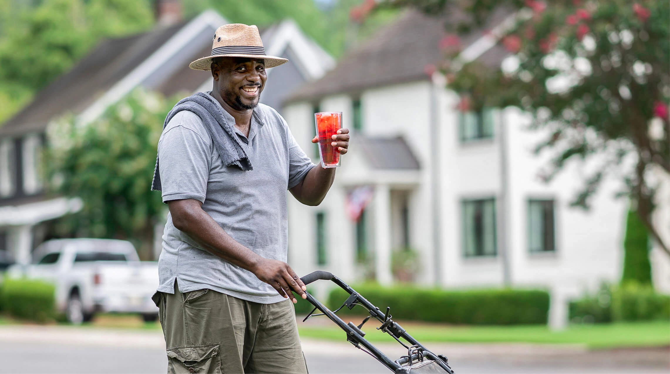 A man mowing his grass while holding a glass of red Sqwincher