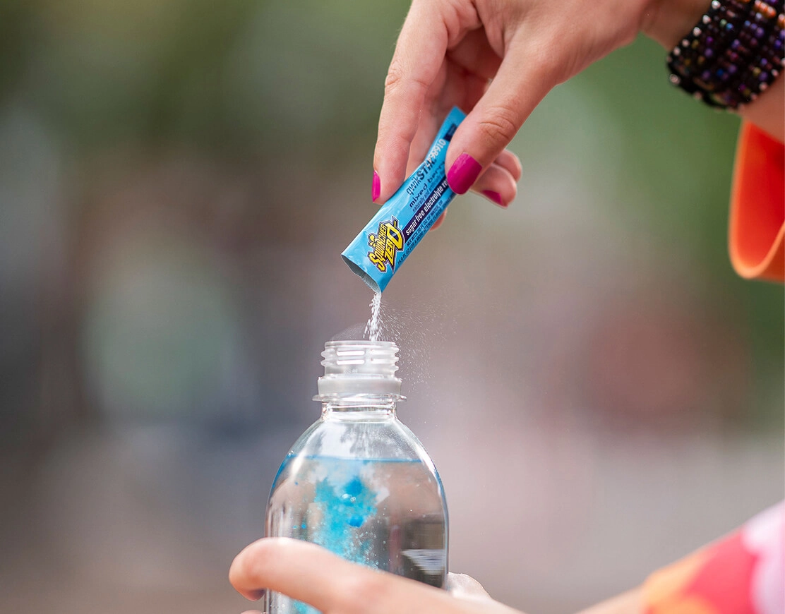 A hand pouring a packet of Sqwincher into a bottle of water