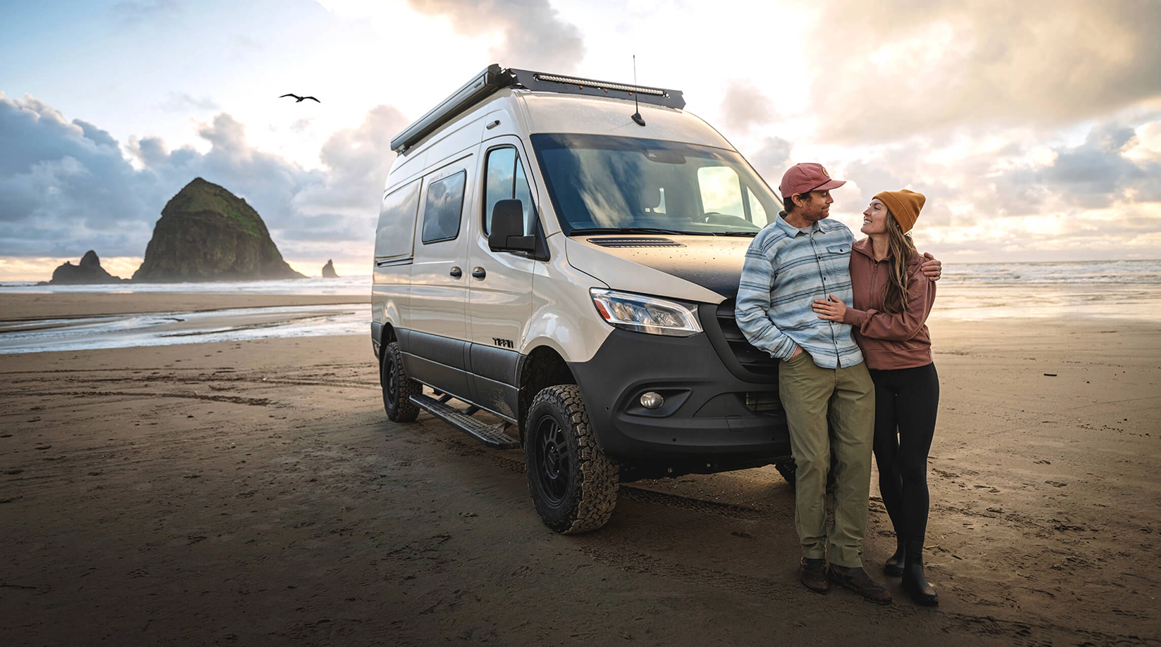 A couple standing in front of their Tiffin motorhome on a beach